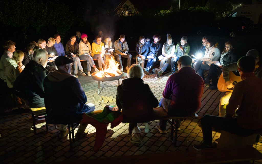 Menschen haben sich sitzend um ein Lagerfeuer versammelt und singen